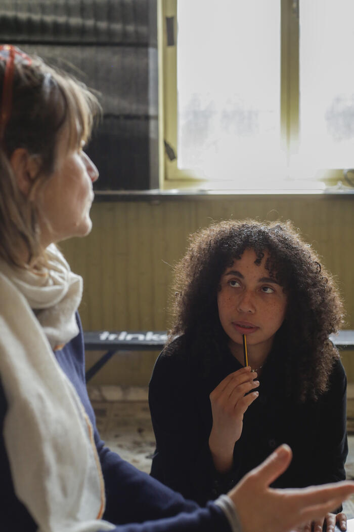 Rafaella looking up at Marie Hélène with a pen in her hand